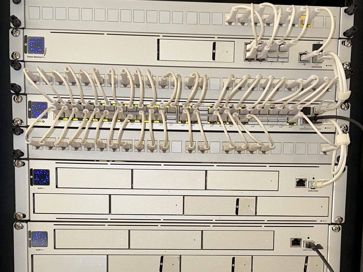 Network rack with UniFi gateway, switches, and recorders, white patch cables neatly dressed